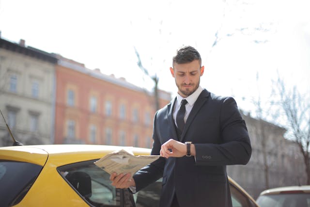 Person wearing a suit, checking their watch and holding a newspaper